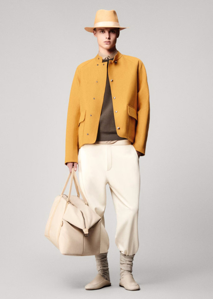 Look issu de la collection printemps-été 2025. Blouson Eliot en lin et soie, pull à col rond The Gif of Kings, pantalon Como en coton, sac de sport Wind, chaussettes Treccia en baby cashmere et mocassins Anton Walk en cuir d’agneau.
